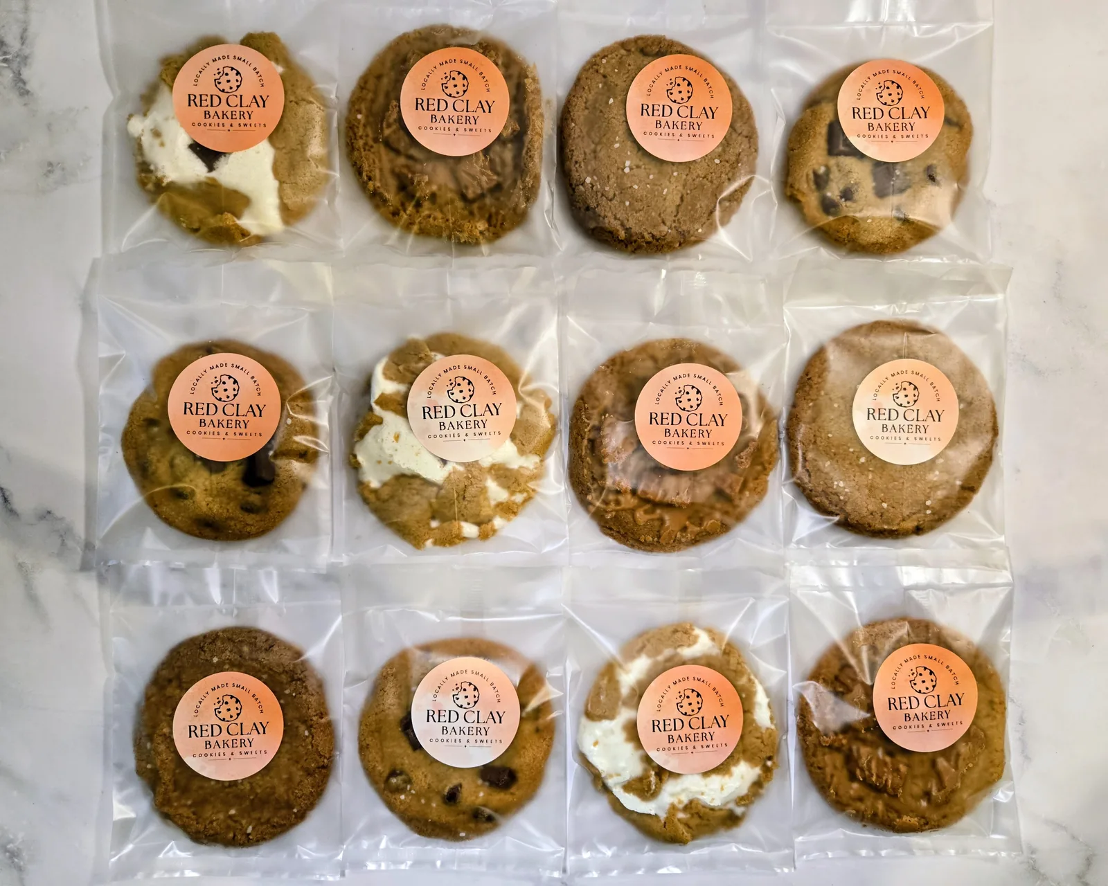 A dozen individually wrapped cookies with Red Clay Bakery labels